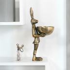 Decorative brass hare figurine holding a bowl, displayed on a modern white shelf with a small deer ornament nearby