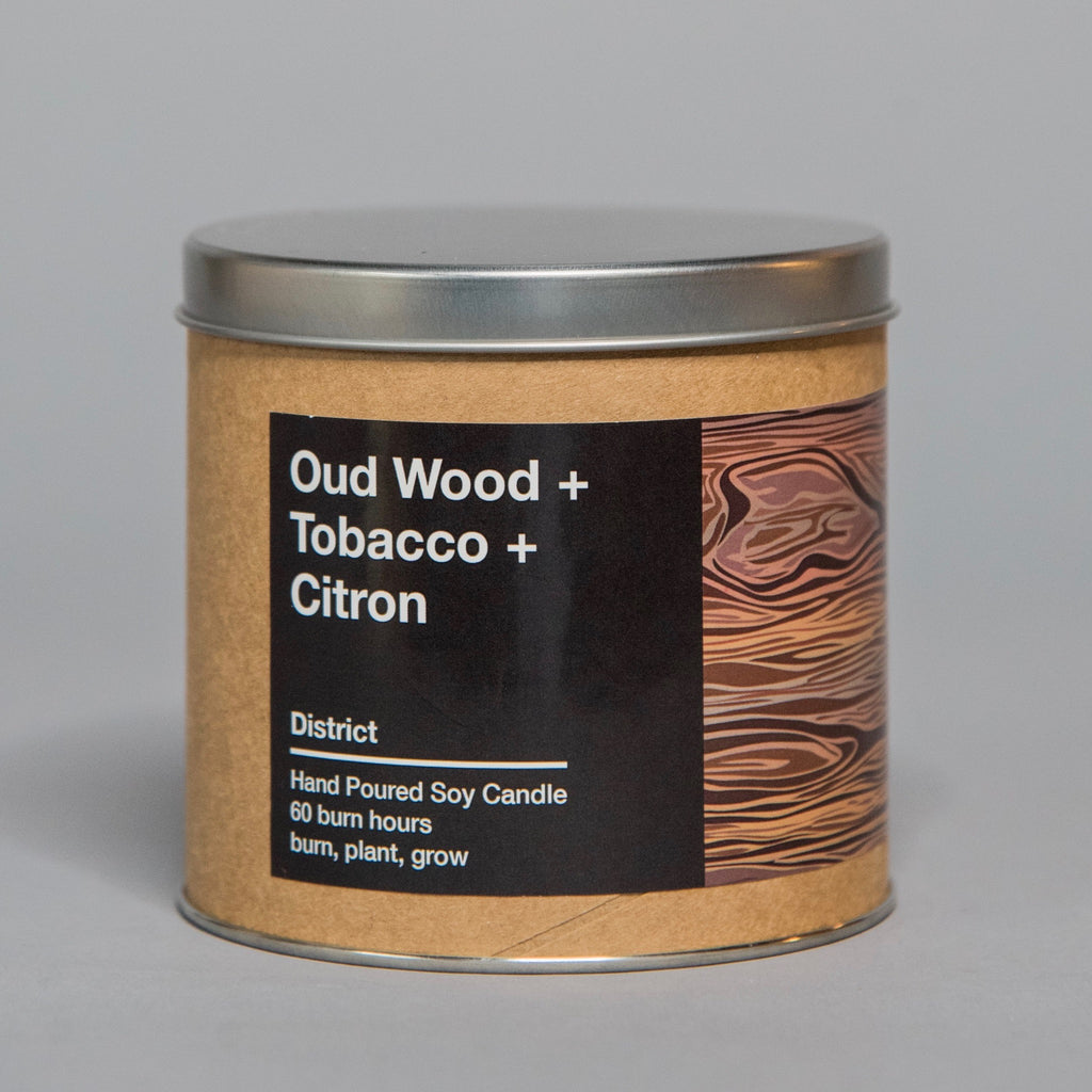 Hand-poured soy candle in metal tin featuring oud wood, tobacco, and citron scents with woodgrain label design