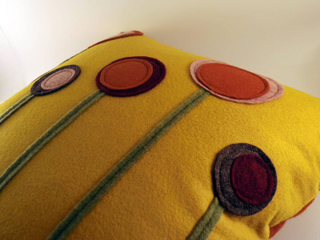 Close-up of a yellow wool felt pillow with colorful layered flower designs and green stems for home decor.