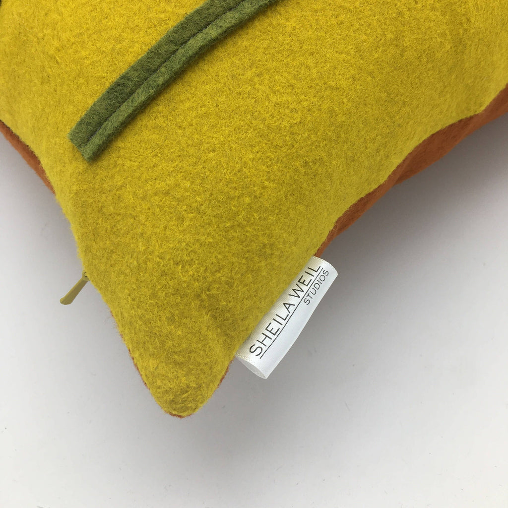 Close-up of a yellow wool felt pillow corner with green felt flower detail and fabric designer tag visible