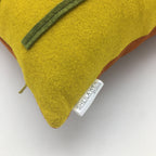 Close-up of a yellow wool felt pillow corner with green felt flower detail and fabric designer tag visible