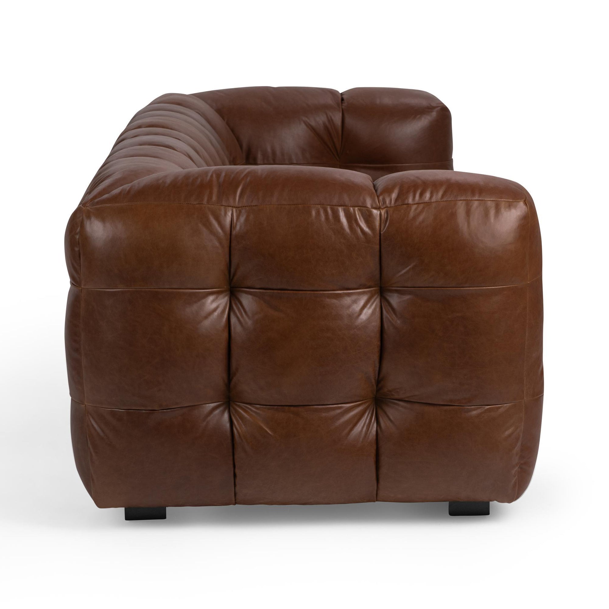 Brown tufted leather sofa with a modern, plush design and deep cushioning viewed from the side.