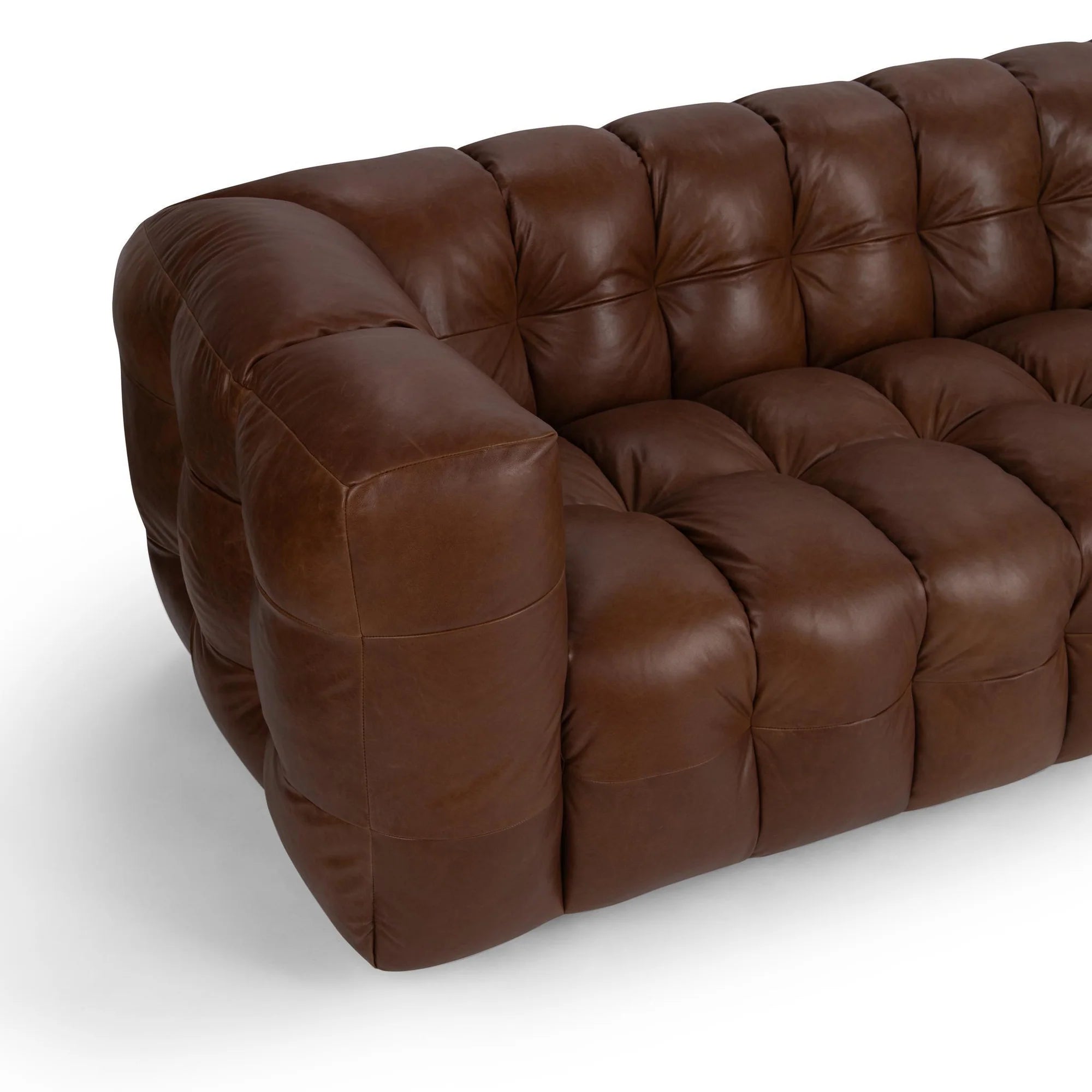Close-up of plush brown leather sofa with deep tufting and rounded, padded armrest in a modern design