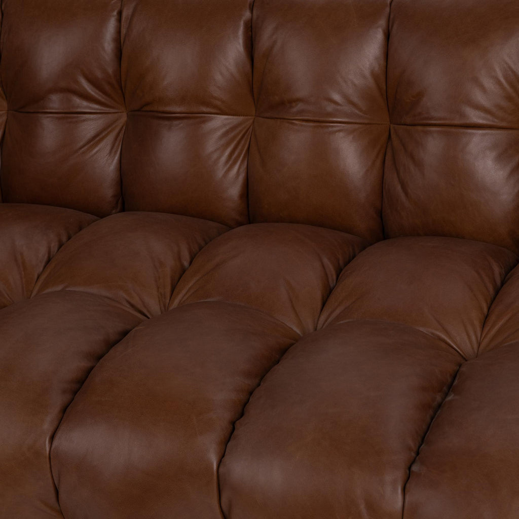 Close-up of a tufted brown leather sofa cushion showing soft, padded upholstery and detailed stitching.