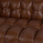 Close-up of a tufted brown leather sofa cushion showing soft, padded upholstery and detailed stitching.