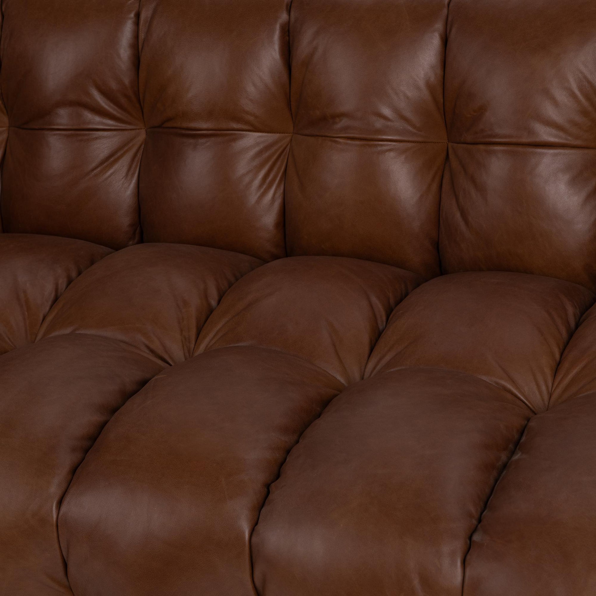 Close-up of a tufted brown leather sofa cushion showing soft, padded upholstery and detailed stitching.