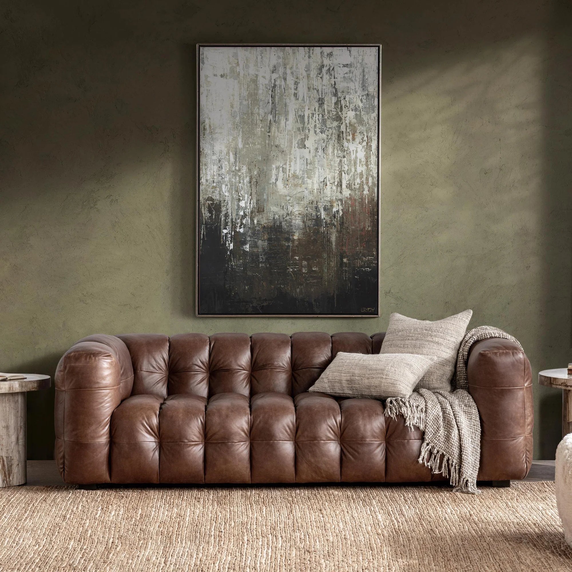 Brown tufted leather sofa with textured pillows and a blanket in a modern living room with abstract wall art