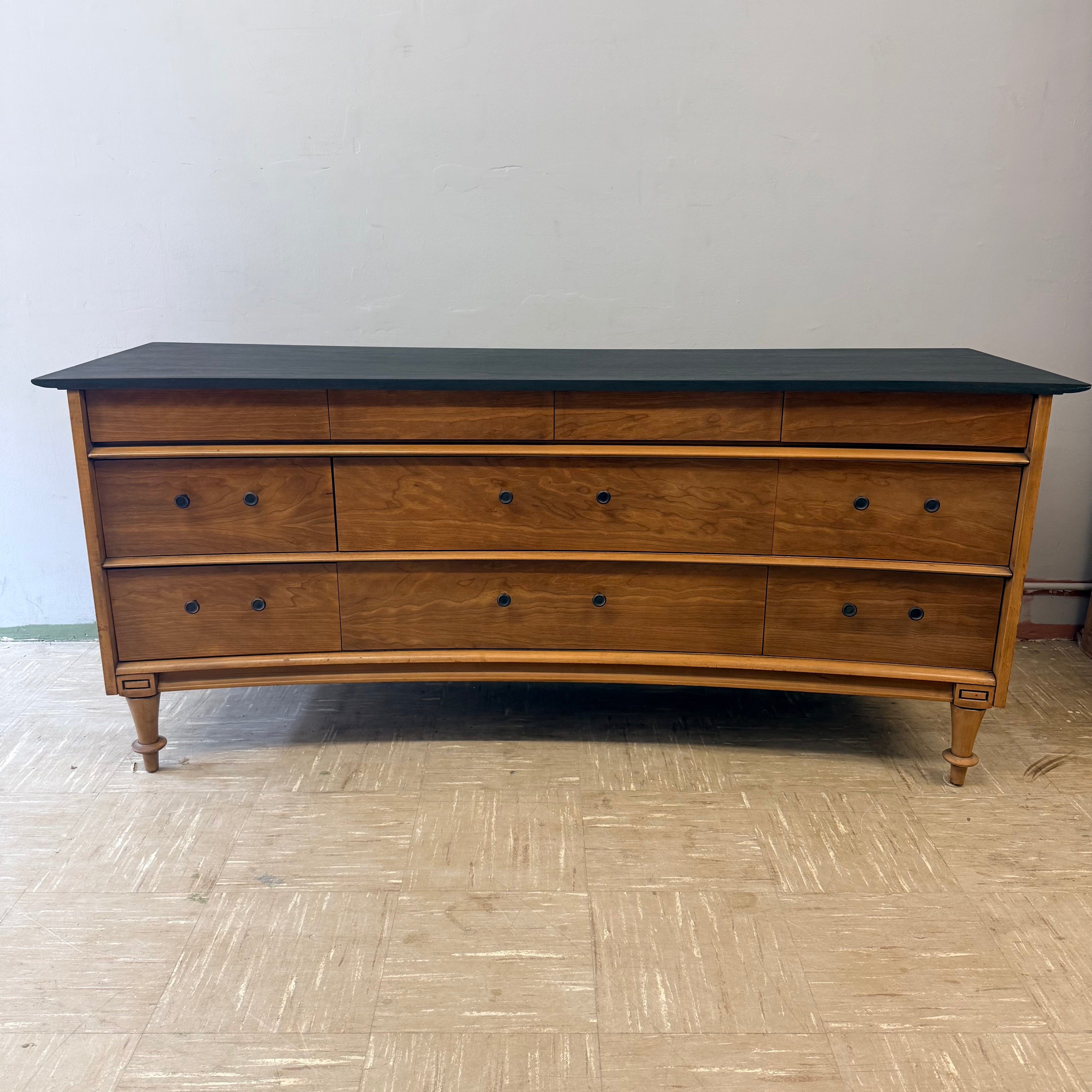 Vintage wooden dresser with curved front and ebony top featuring multiple drawers and simple round knobs.