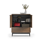 Wooden entry cabinet with open doors displaying organized shelves holding books, binoculars, a hat, and decorative items.