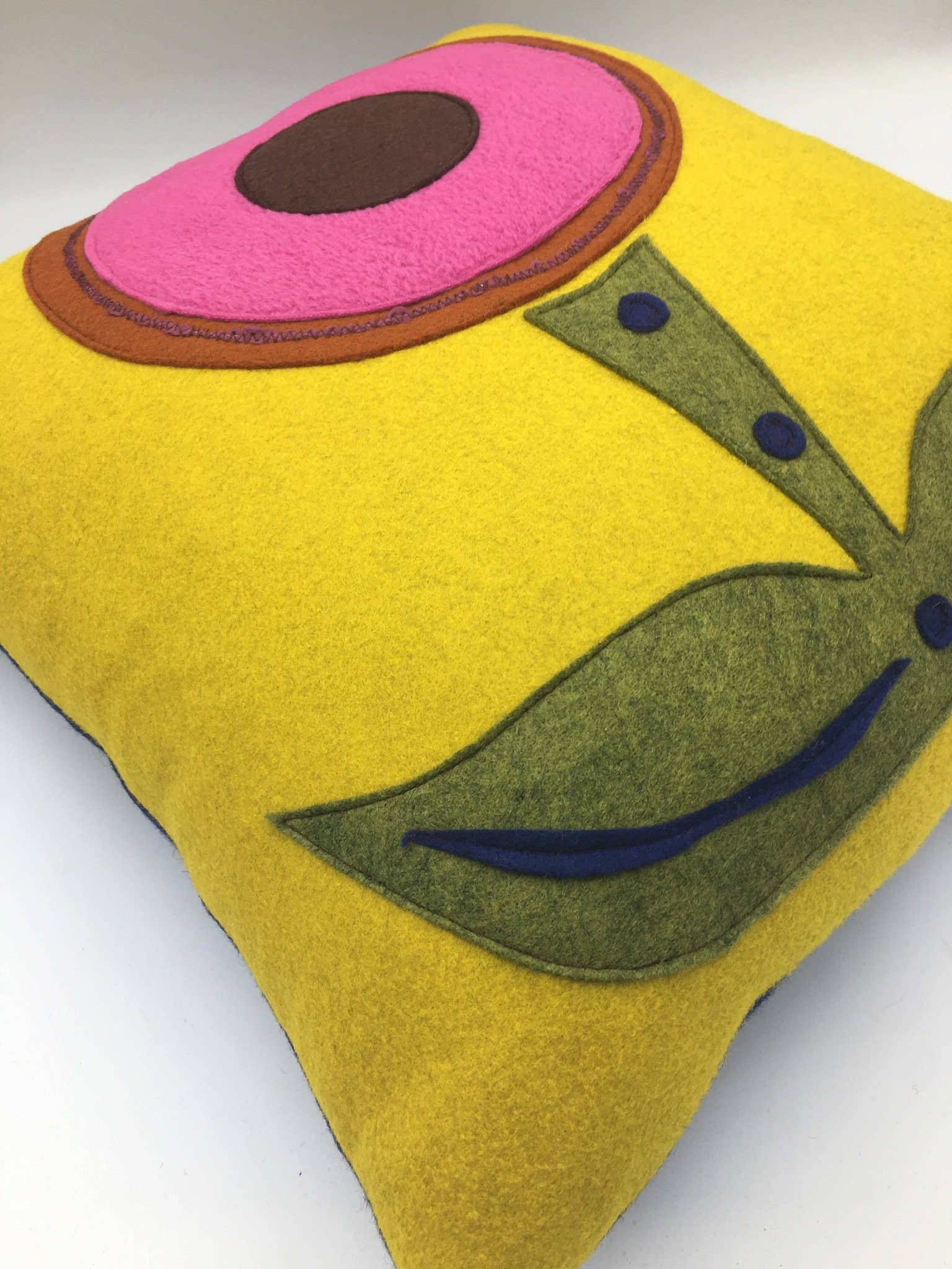 Yellow wool felt pillow with abstract pink and brown flower design and green leaf accents on home decor pillow.
