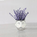 Ceramic planter shaped like a bearded man's face holding a bunch of purple lavender flowers.