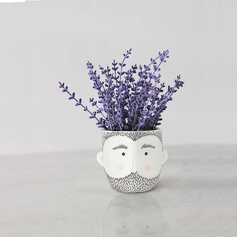Ceramic planter shaped like a bearded man's face holding a bunch of purple lavender flowers.