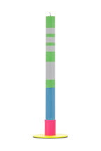 Tall colorful candle with green, white, blue, and pink sections on a yellow metal holder against a white background