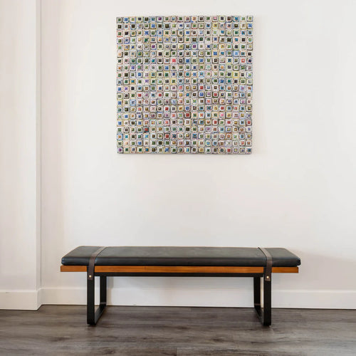 Modern black leather bench with wooden frame and metal legs against a white wall with colorful artwork above