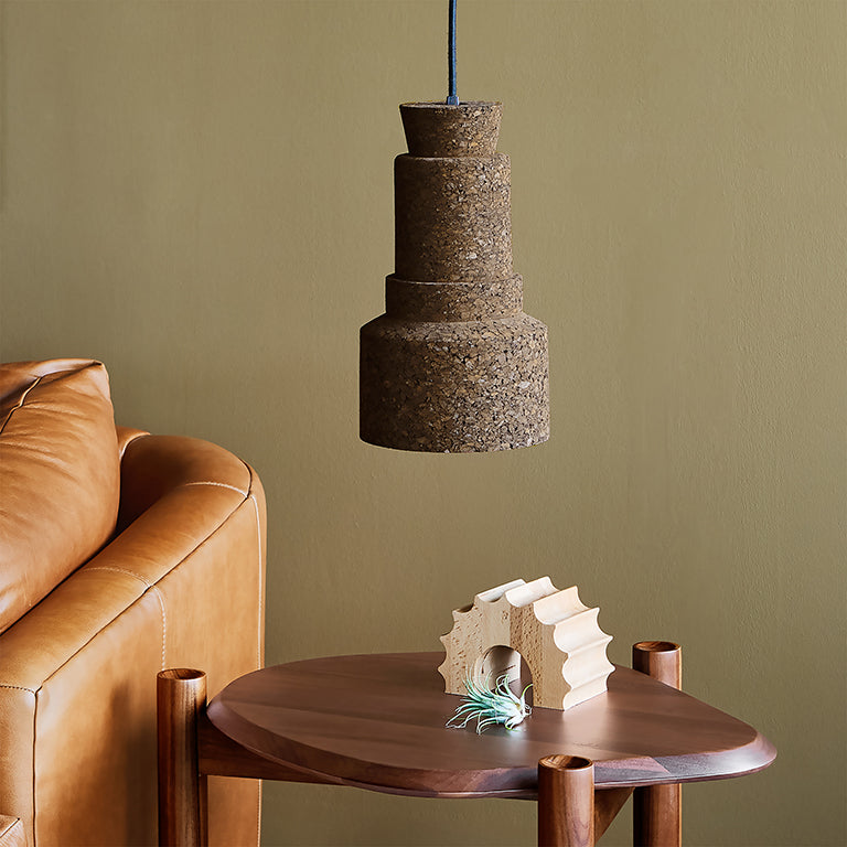 Small pendant light made from cork with a modern design hanging above a wooden side table and leather sofa