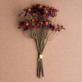 Bundle of deep red faux chamomile flowers with yellow centers against a neutral brown background for home decor