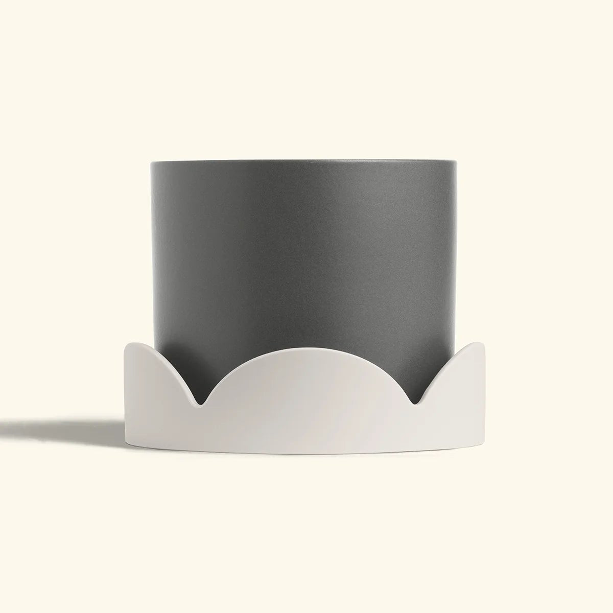Matte grey planter set inside a beige petal-shaped drip tray on a cream background.