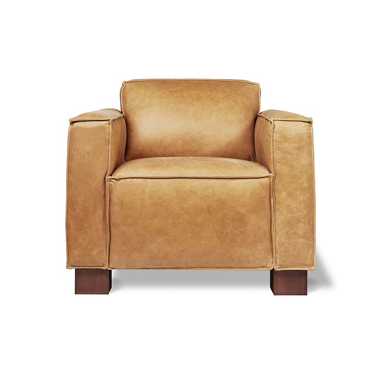 Tan leather armchair with wide cushioned arms and wooden block legs, modern furniture design.