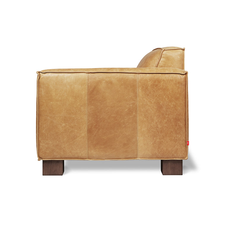 Side view of a modern leather chair with a smooth caramel finish and wooden block legs.