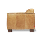 Side view of a modern leather chair with a smooth caramel finish and wooden block legs.