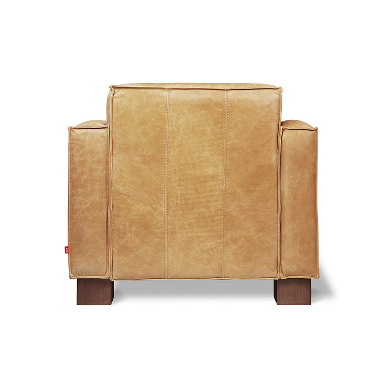 Back view of a tan leather armchair with wide padded arms and wooden legs on a white background