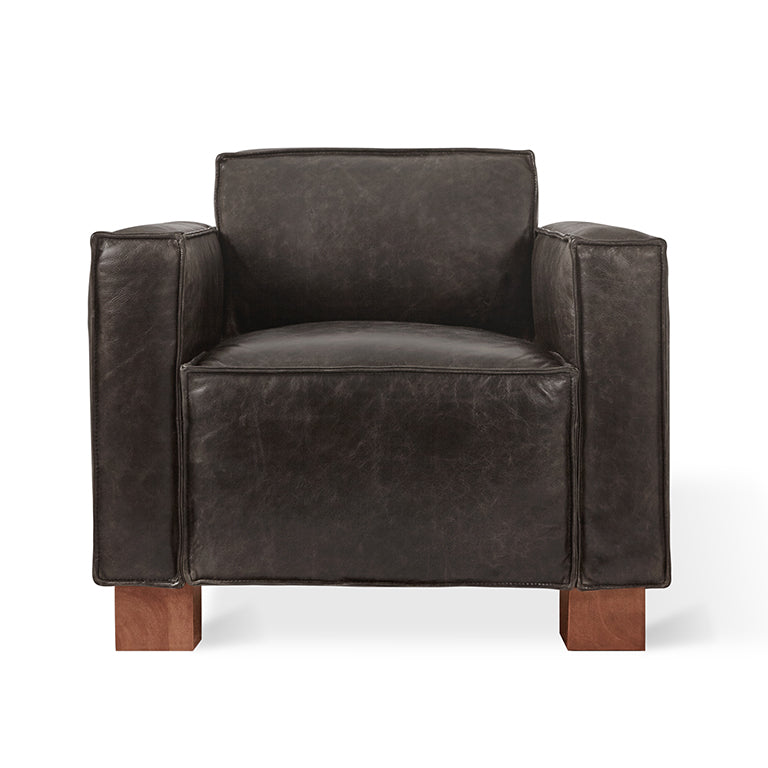 Modern dark leather armchair with wide armrests and wooden block legs in contemporary style
