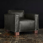 Black leather modern armchair with wooden block legs on a rustic textured floor background