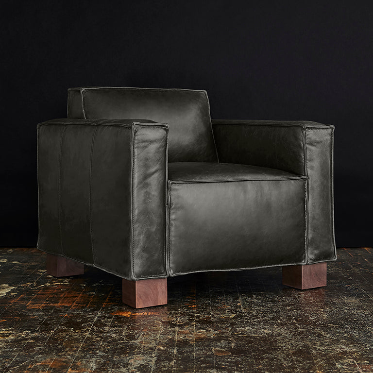 Black leather modern armchair with wooden block legs on a rustic textured floor background
