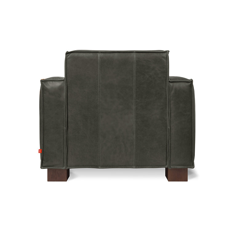 Rear view of a dark leather lounge chair with wide arms and wooden block legs on a white background