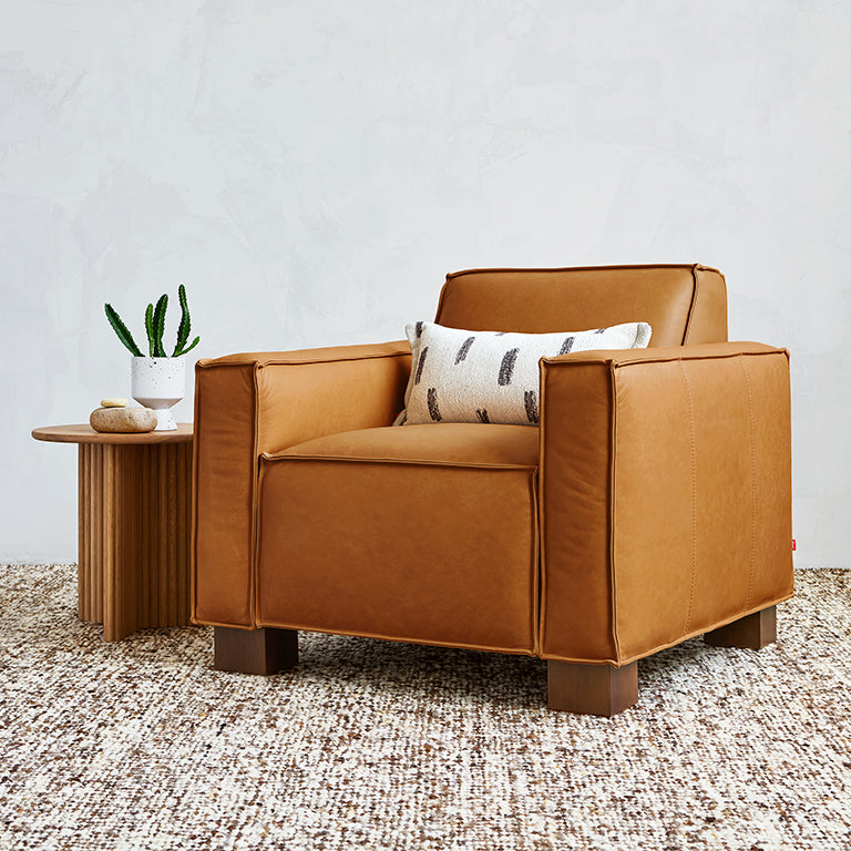 Leather armchair with a modern boxy design, paired with a small wooden side table and decorative pillow.