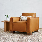 Leather armchair with a modern boxy design, paired with a small wooden side table and decorative pillow.