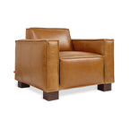Modern midcentury style leather armchair with wide arms and dark wooden block legs in warm brown tone