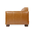 Side view of a modern tan leather chair with wooden block legs and clean stitch detailing