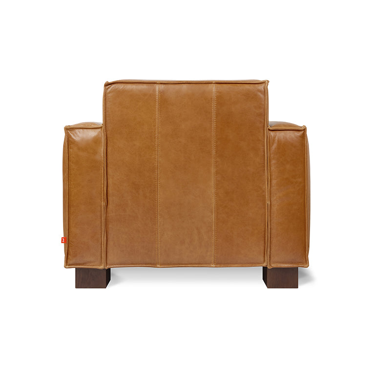 Rear view of a caramel brown leather chair with wide armrests and dark wooden legs