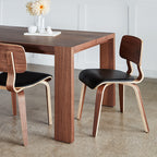 Two modern dining chairs with curved walnut backs and black leather seats next to a matching wood table.