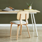 Light wood dining chair with curved backrest and white cushioned seat paired with a minimalist wooden desk and plant decor