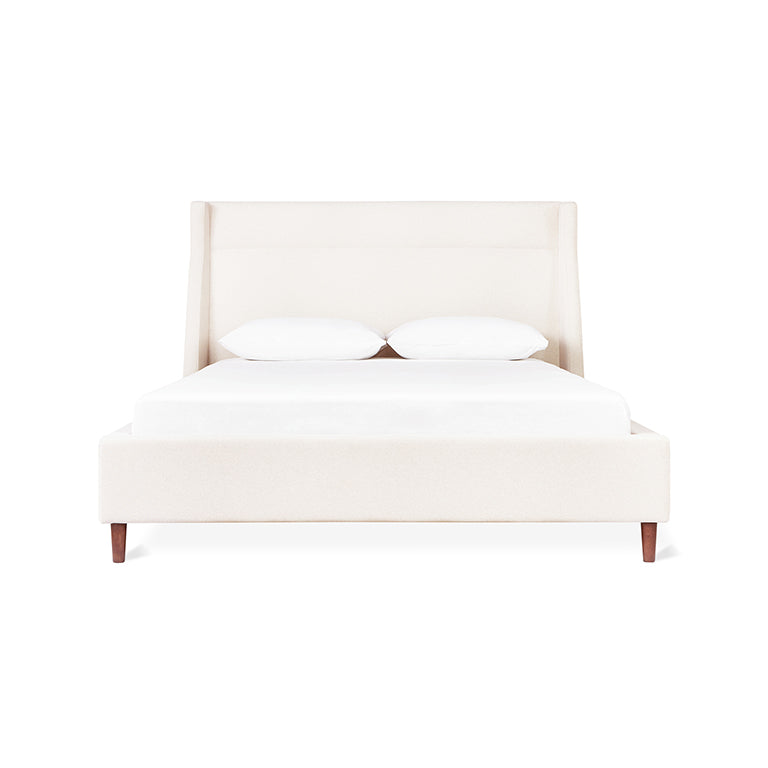 Cream-colored fabric bed with tall upholstered headboard and wooden legs, styled with white bedding and pillows