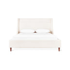 Cream-colored fabric bed with tall upholstered headboard and wooden legs, styled with white bedding and pillows