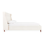 Side view of a modern cream upholstered bed with a tall wingback headboard and wooden legs