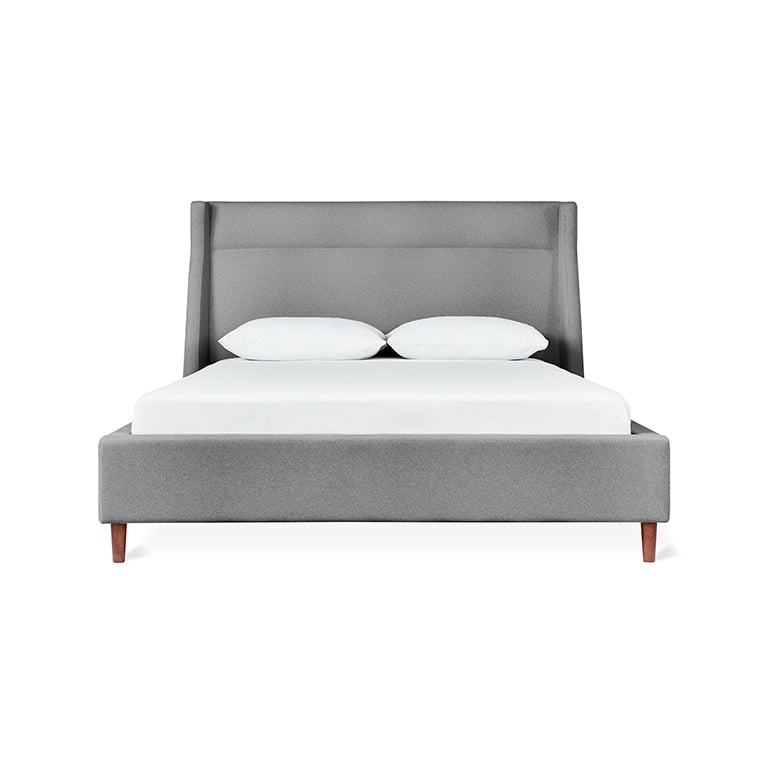 Modern gray upholstered bed with angled headboard and wooden legs, styled with white bedding and pillows