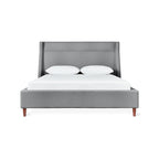 Modern gray upholstered bed with angled headboard and wooden legs, styled with white bedding and pillows