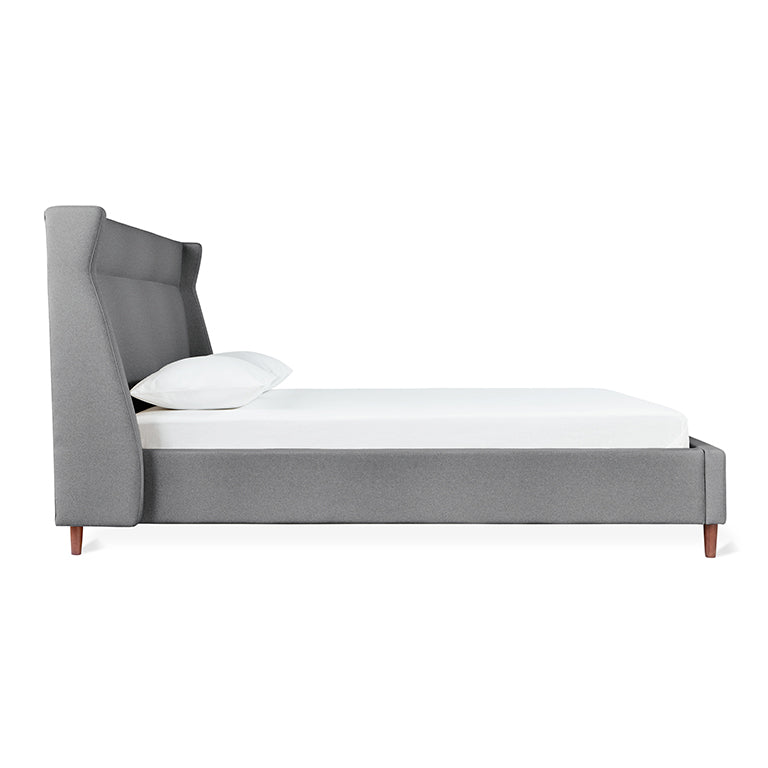 Side view of a contemporary gray upholstered bed frame with tall padded headboard and wooden legs