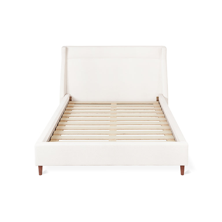 Minimalist upholstered bed frame with wooden slats and a high padded headboard in neutral fabric