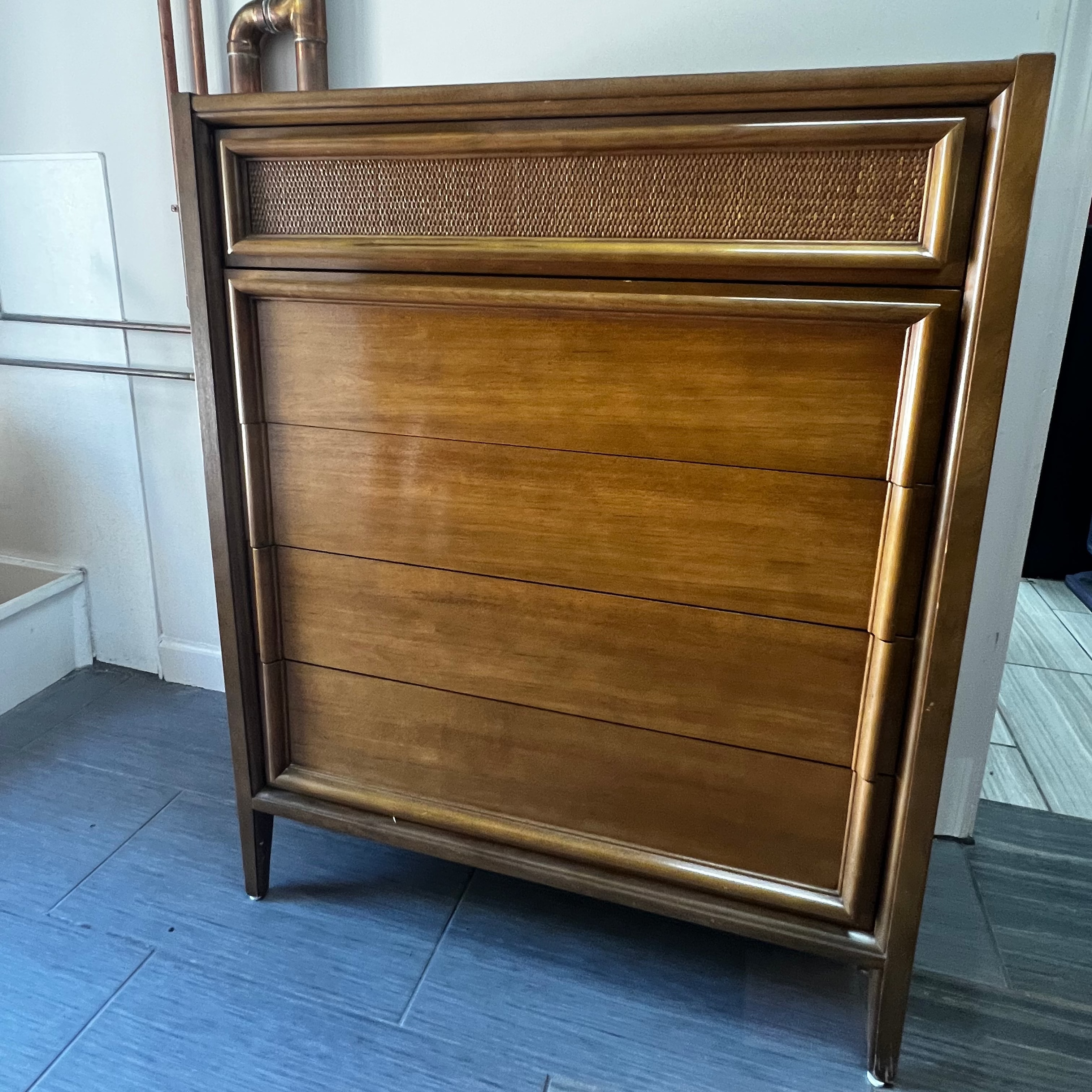 Wooden dresser with wicker accents on a tiled floor.