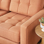 Close-up of a tufted burnt orange fabric sectional sofa armrest next to a wooden side table with a small potted plant