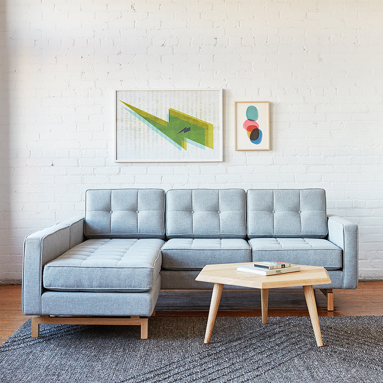 Light gray midcentury modern sectional sofa with tufted cushions next to a wooden coffee table on a textured rug