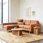 Orange upholstered bi-sectional sofa with tufted cushions in a modern living room setting with wooden tables and artwork