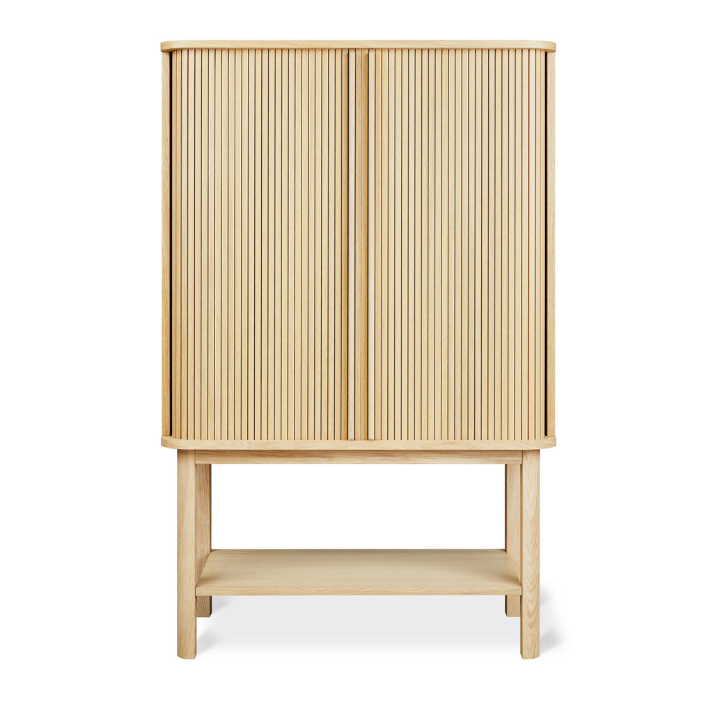 Wooden tall cabinet with vertical slatted doors and open lower shelf in a light oak finish