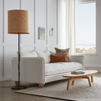Modern floor lamp with wood veneer shade next to white sofa and wooden coffee table in bright living room
