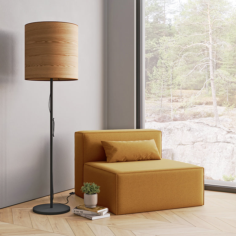 Minimalist floor lamp with wooden shade beside mustard modern lounge chair by large window and small plant on books